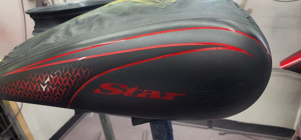 Close-up of a black motorcycle fuel tank with a glossy red design. The word "Star" is prominently displayed in red, accompanied by a subtle star emblem. The design features a red geometric pattern on the side.