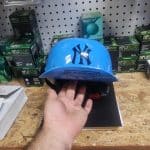 A hand holds a blue helmet with a logo and the word "SLINGSHOT" on the visor. The helmet is displayed on a wooden surface, surrounded by boxes on a shelf.