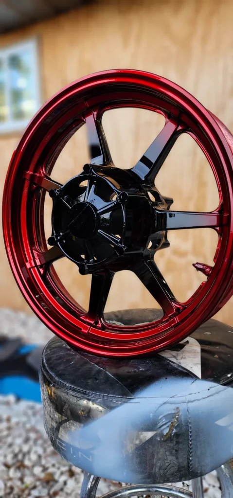 Same candy-red and black wheel photographed straight-on showing deep gloss reflections, sitting on a stool outside