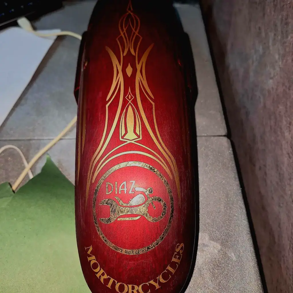 A maroon motorcycle part with gold designs features “DIAZ MOTORCYCLES” and a motorcycle graphic.