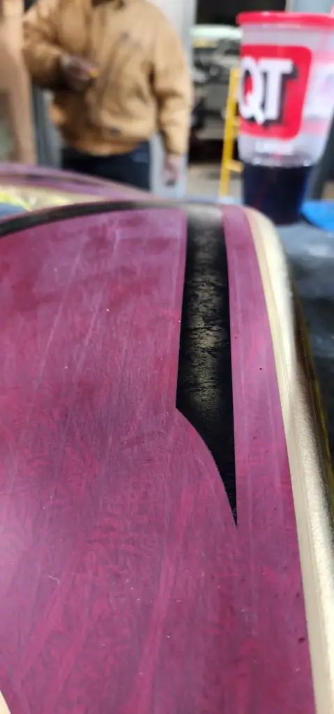 Close-up of maroon and black painted surface with gold trim; people and a drink blur in background.