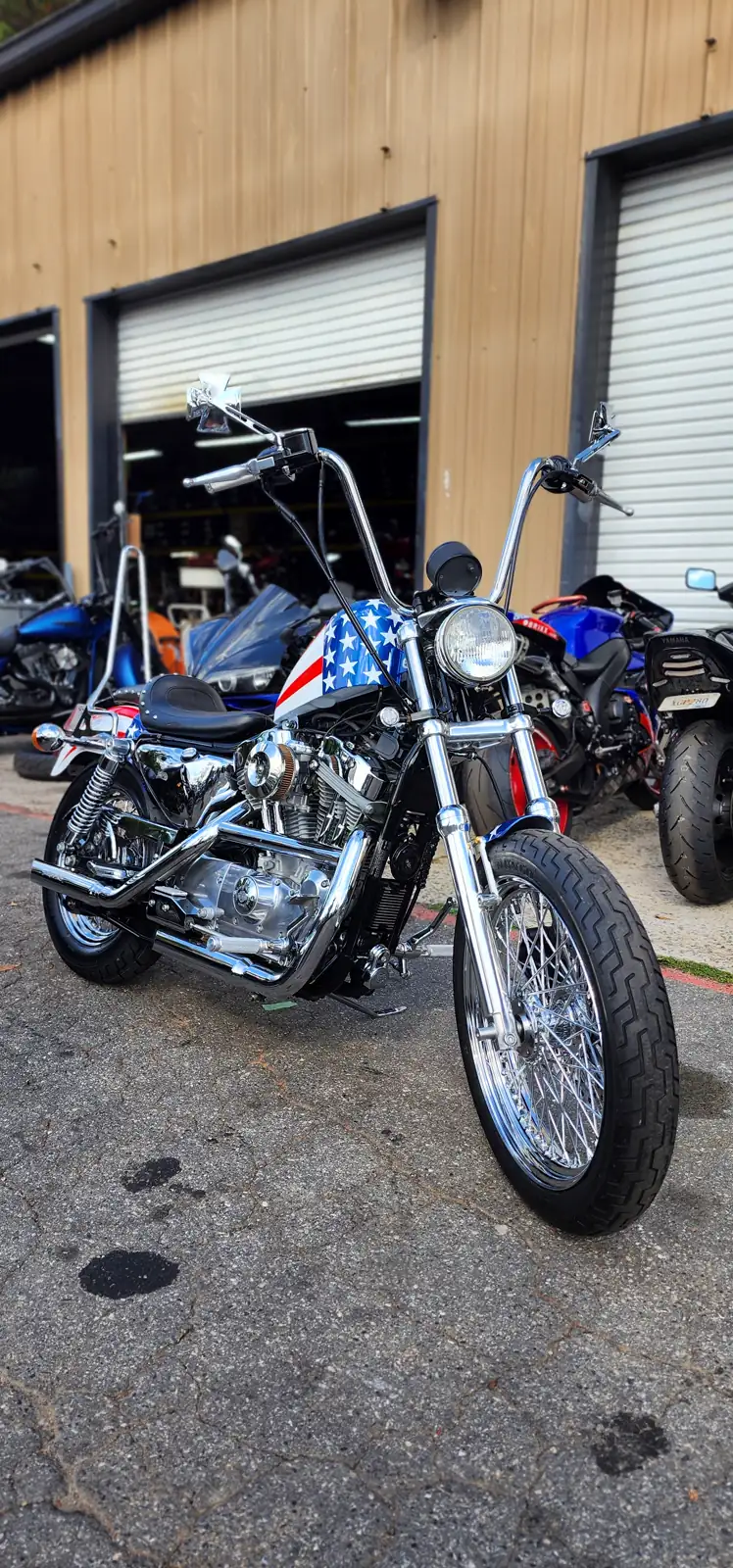 custom paint cost Douglasville — American-flag-painted Harley Sportster chopper with ape hangers outside the shop bays