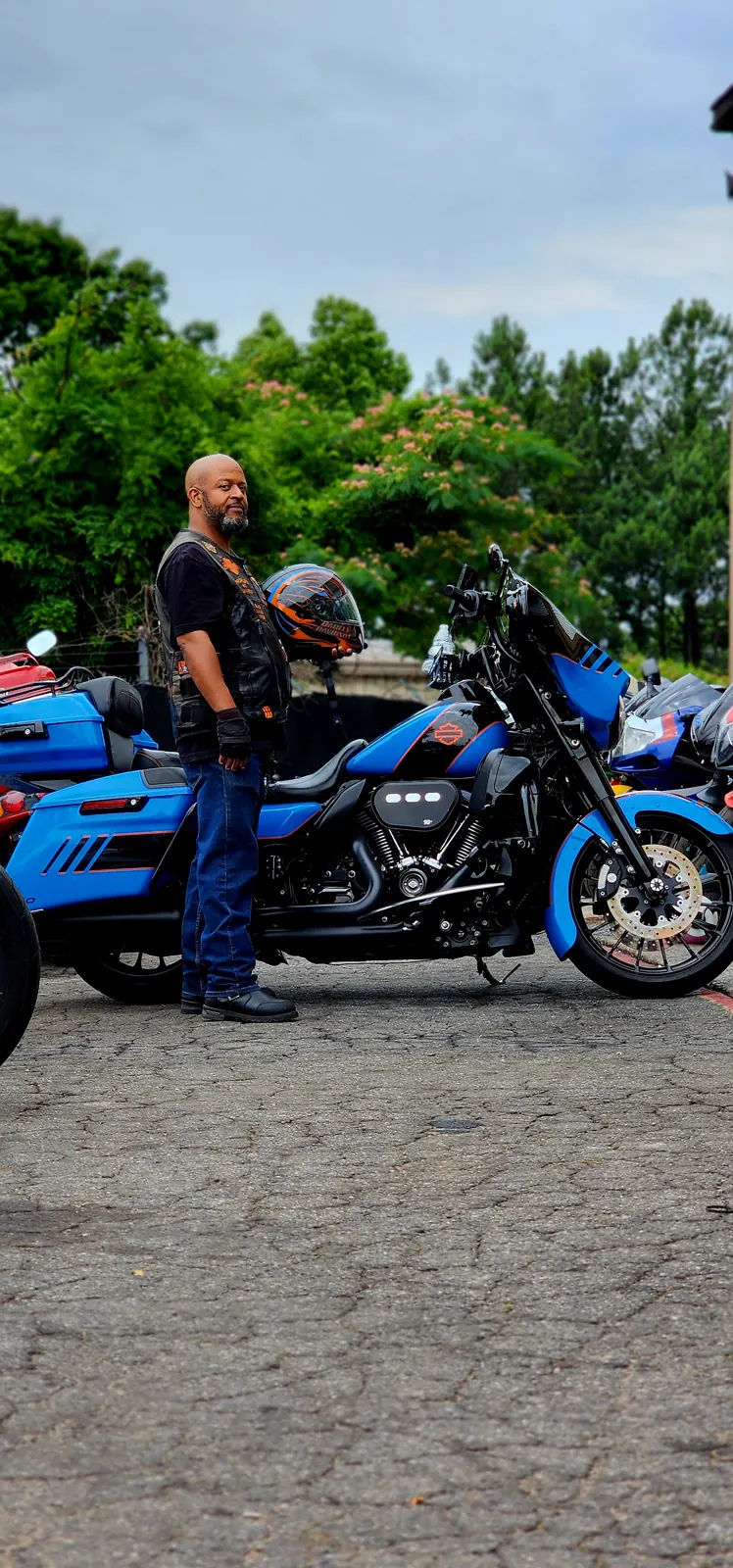 Full side profile of the custom blue and orange Harley bagger with the owner holding his matching helmet, blue trike behind.