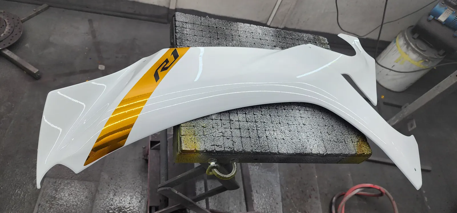 matte vs gloss paint Douglasville — gloss white Yamaha R1 side fairing panel with a gold stripe on a padded stand