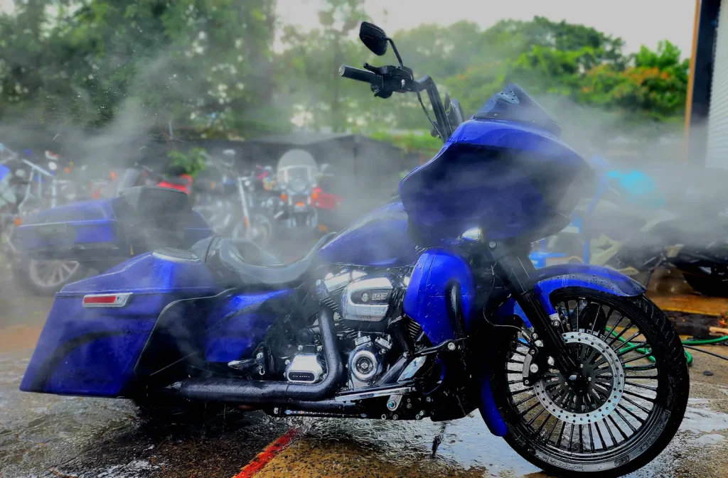 Blue Harley Road Glide mid-wash with heavy spray mist, side profile showing wet paint, chrome engine and fat spoke front wheel.