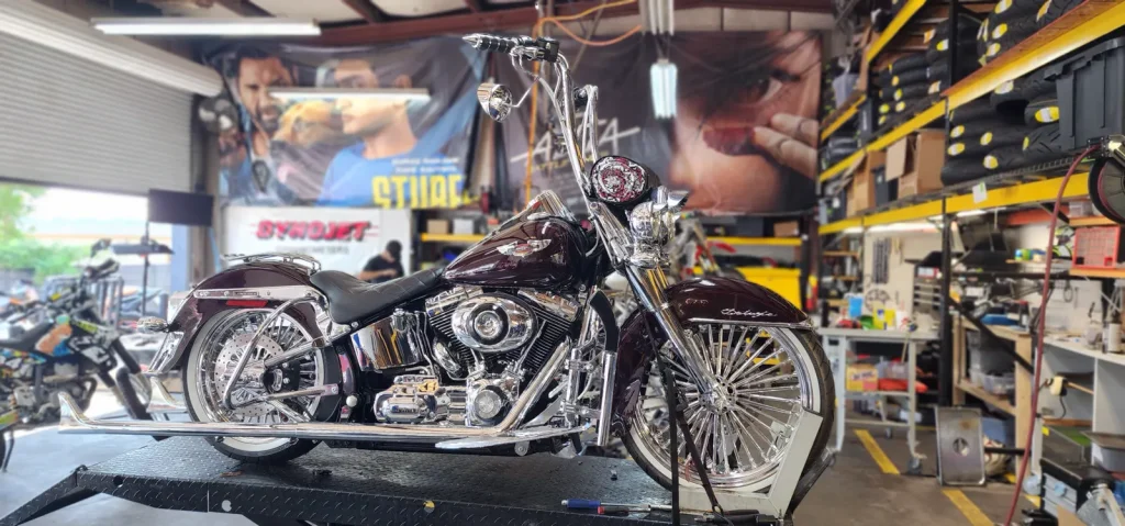 Deep burgundy Harley-Davidson Softail Deluxe with heavy chrome, spoked wheels and ape hangers sitting on a lift table in the shop.