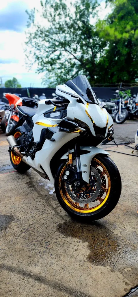 Front three-quarter of the freshly washed white Honda CBR1000RR with gold wheels, water still beading on the bodywork.