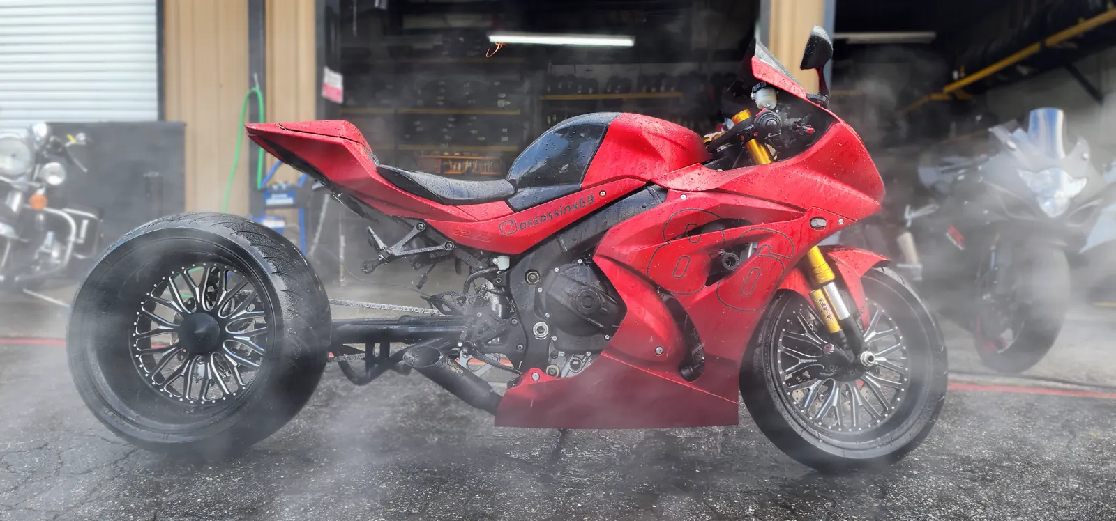 custom paint Sandy Springs — red fat-tire Suzuki GSX-R being rinsed outside the shop bay in heavy water mist