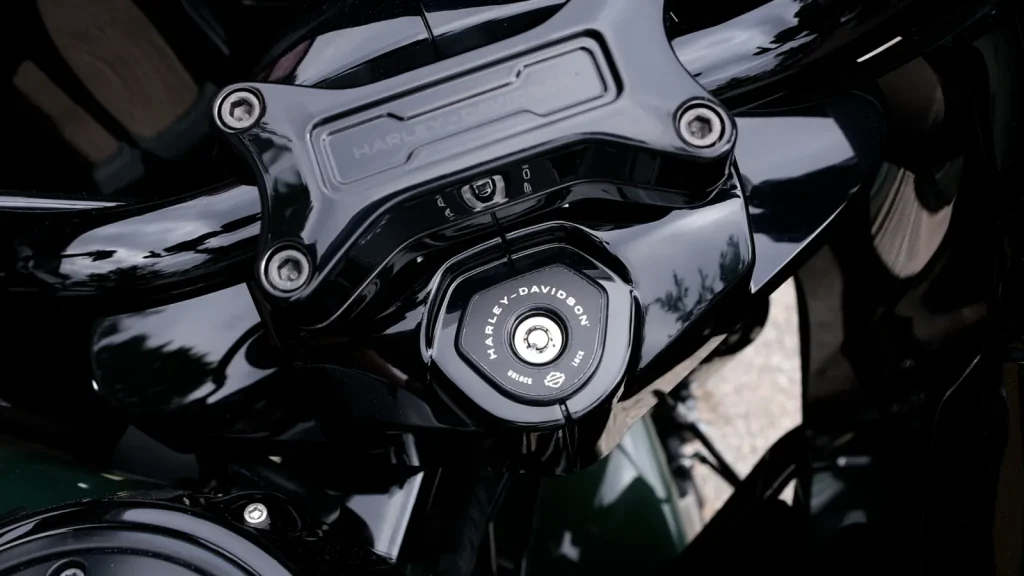 Tight close-up of a glossy black Harley-Davidson top triple clamp and ignition switch with mirror-like reflections in the paint and chrome.