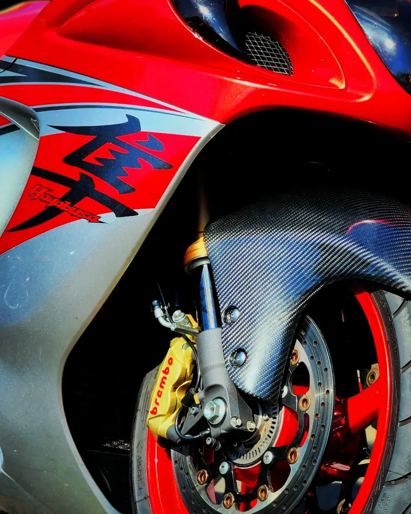 Tight close-up of a red and silver Suzuki Hayabusa front end showing glossy fairing graphics, yellow Brembo caliper, carbon fender and drilled rotor.
