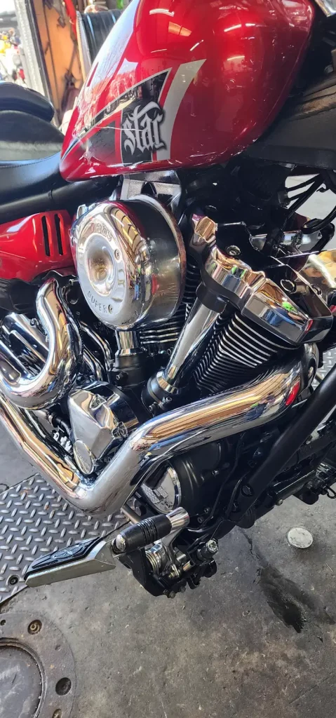 Tight close-up of a red Yamaha Star cruiser's polished chrome V-twin engine, air cleaner cover and exhaust headers with mirror-like reflections.