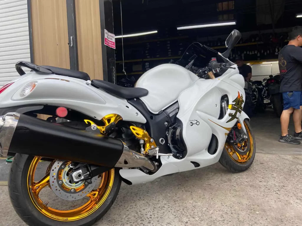 A white Suzuki Hayabusa with gold wheels, gold rearsets and kanji graphics sits gleaming at the shop bay door.