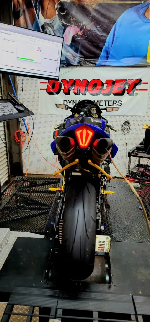 A blue sport motorcycle’s rear view on a Dynojet dyno testing platform with monitors and cables visible.