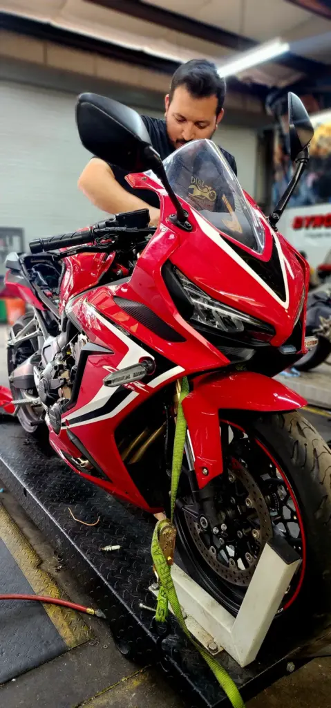 Man adjusting handlebars on a red sport motorcycle in a garage, focused on maintenance work.