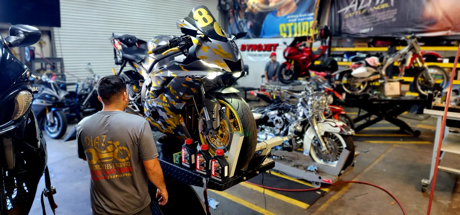 Motorcycle service East Cobb — Diaz technician beside a camo-wrapped Yamaha R1 on the lift with oil bottles staged