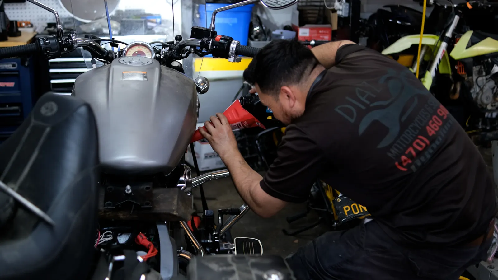 Motorcycle not starting Kennesaw — tech in a Diaz tee pours fluid through a red funnel into a grey naked bike.