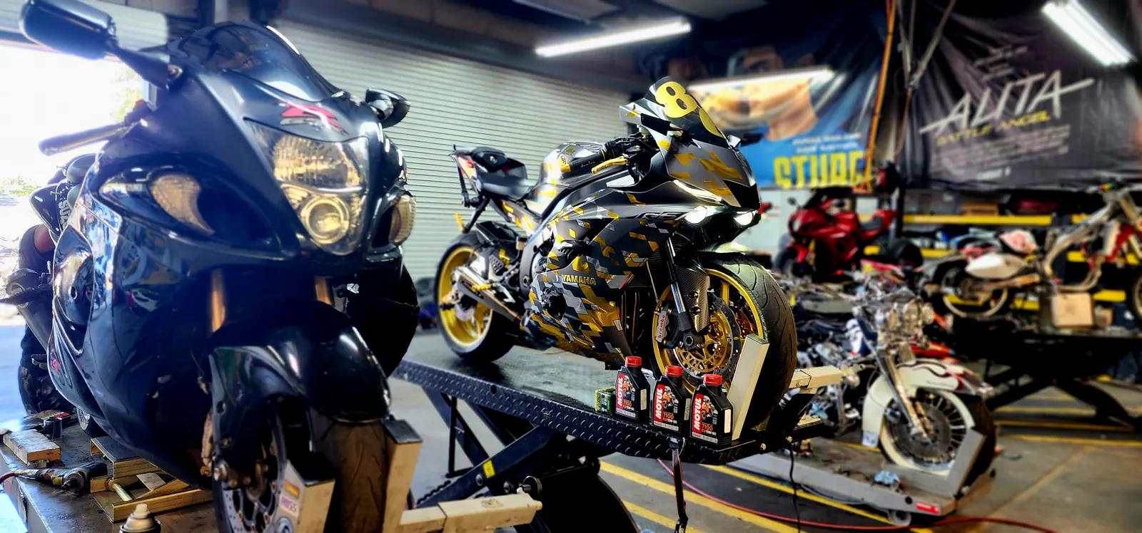 Motorcycle maintenance for Roswell riders — Yamaha R1 in camo wrap on the lift with oil bottles, Hayabusa in front