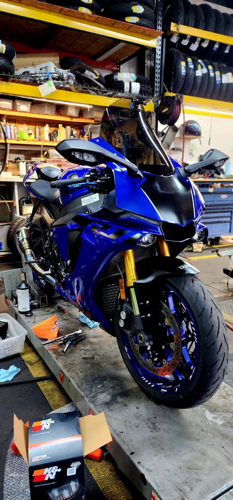 Motorcycle service Marietta — blue Yamaha R1 on a lift with an oil bottle and open air filter box, tires racked behind.