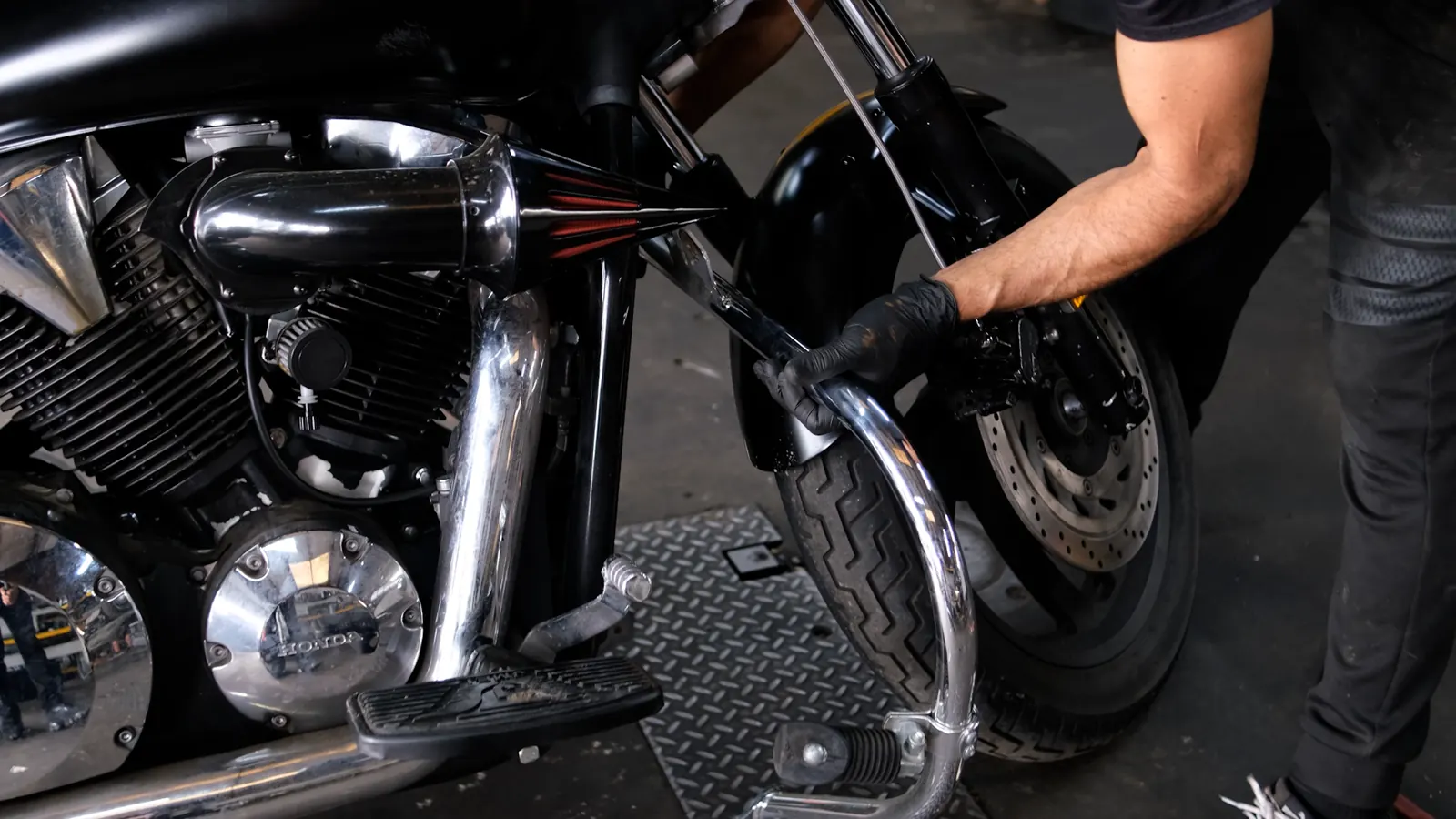 Indie service Marietta — gloved hand working on the front brake caliper and rotor of a black Honda V-twin cruiser