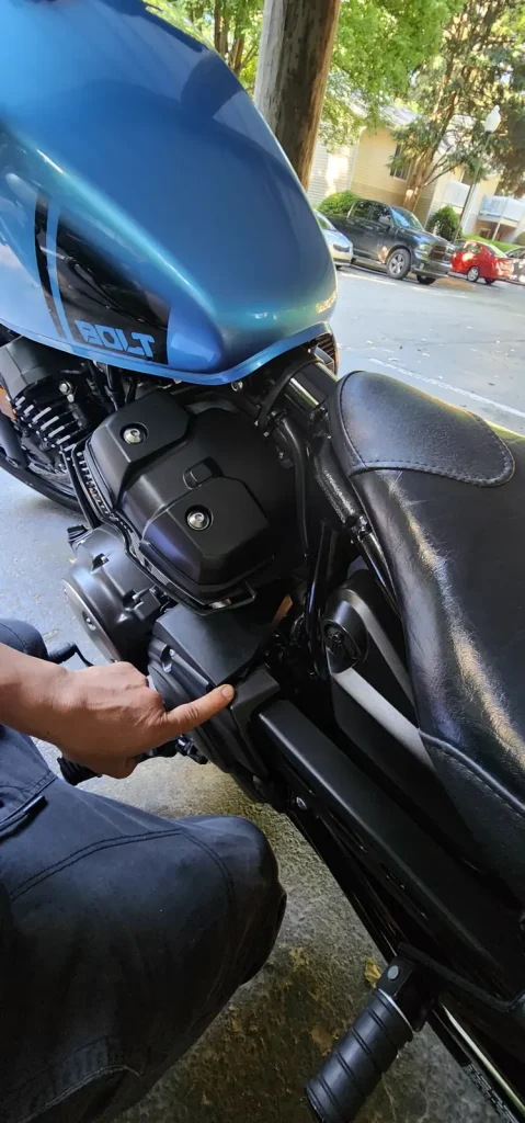 Close-up of a hand reaching into the engine and air-box area of a blue Yamaha Bolt cruiser parked on pavement