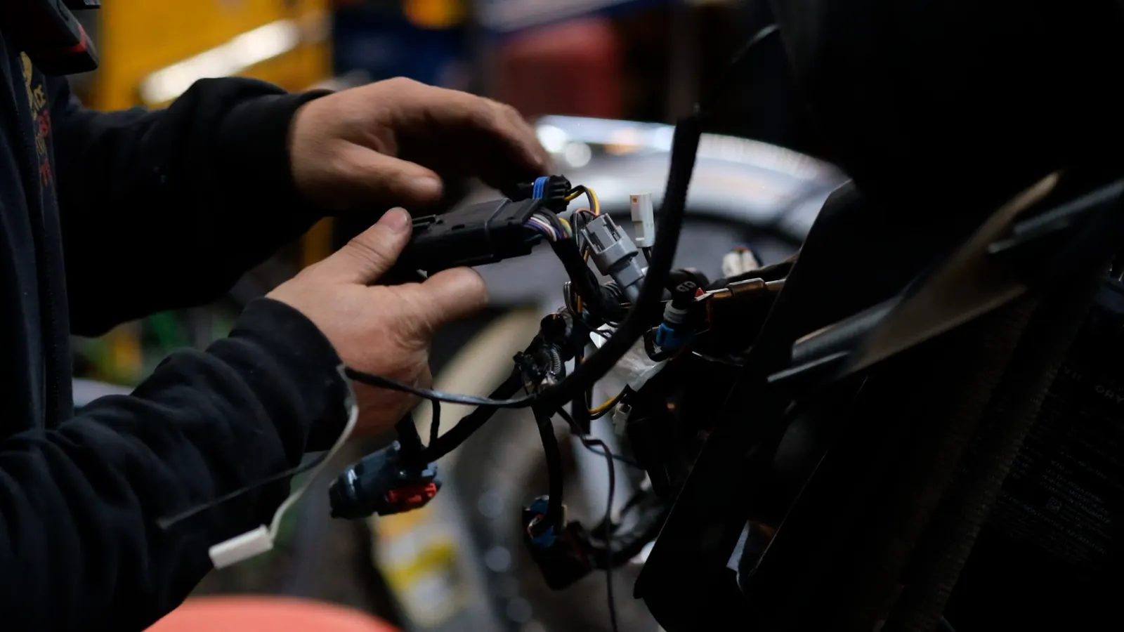 dyno vs stock Powder Springs — hands holding a wiring harness with multiple connectors over a disassembled bike front end