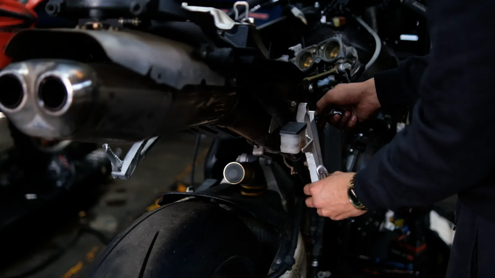 Motorcycle service Cartersville — hands using a wrench at the rear brake master cylinder area of a sportbike.