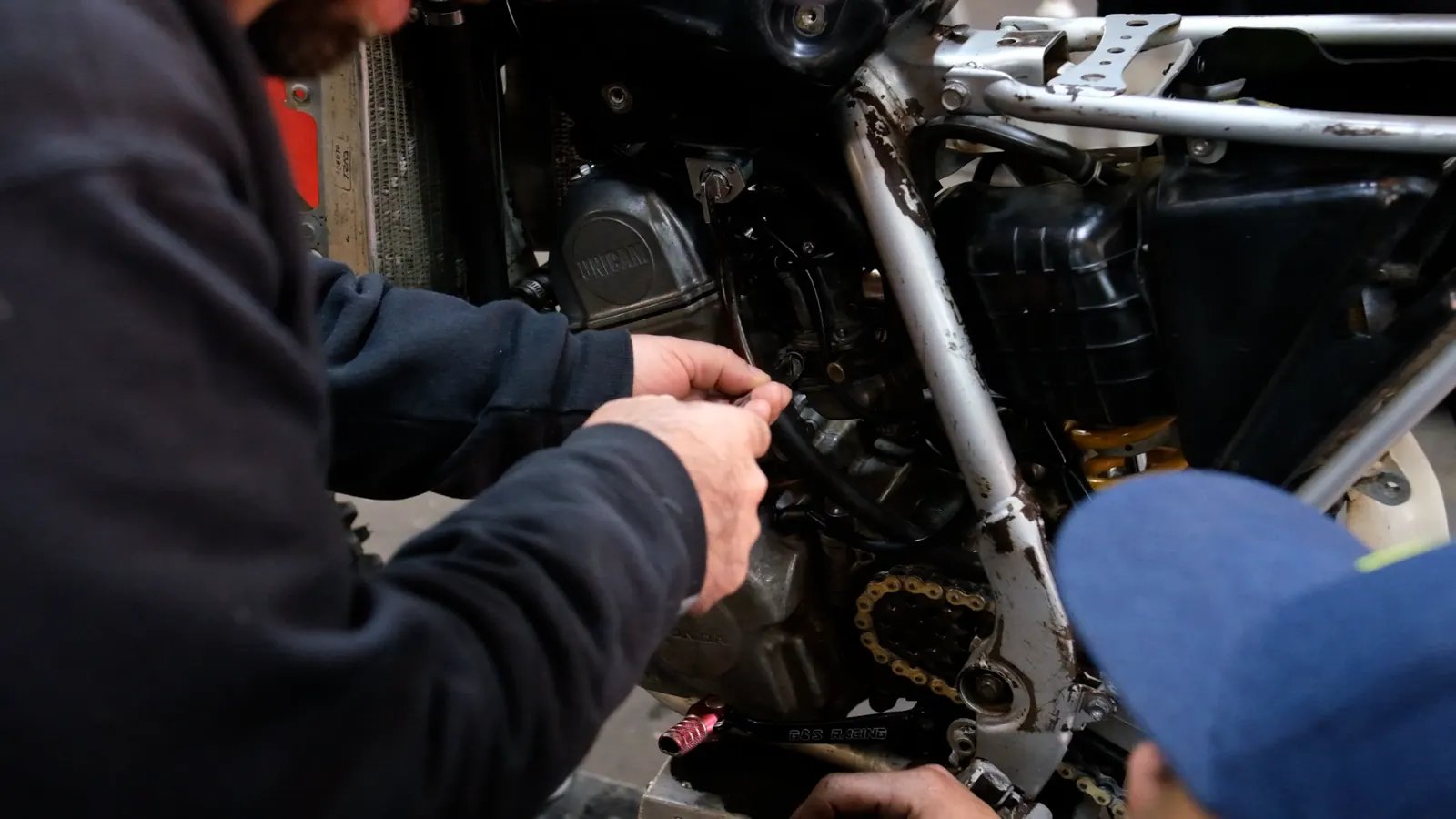 Best motorcycle service Cartersville — technician's hands working on the engine and wiring of a stripped dirt bike frame.