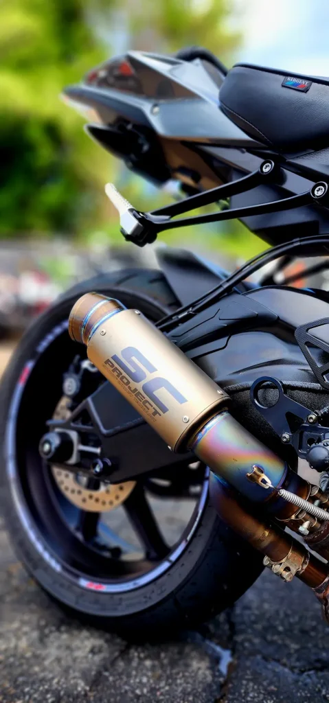 Close-up of a titanium SC Project slip-on exhaust with heat-blued tip mounted on a black sportbike's rear end.