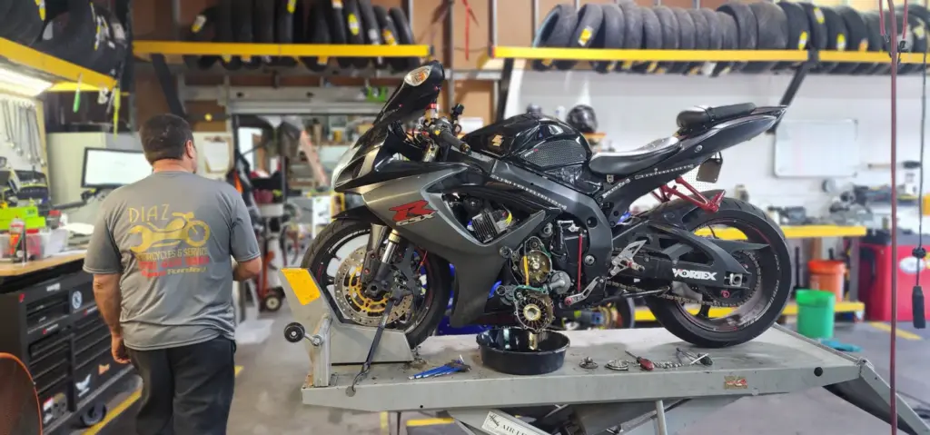 A black sport motorcycle on a lift is being serviced in a workshop, with a man standing nearby.