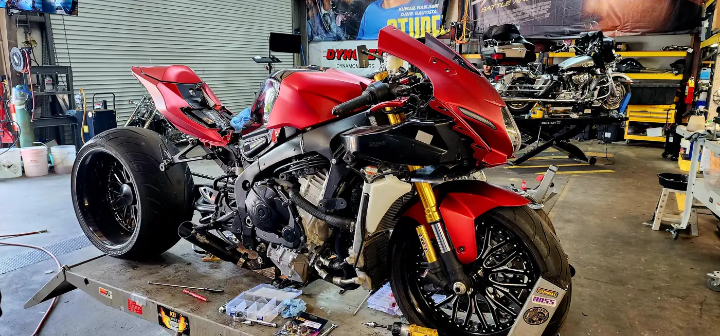 overdue service East Cobb — matte red fat-tire Suzuki GSX-R on a lift table with parts trays and tools spread out