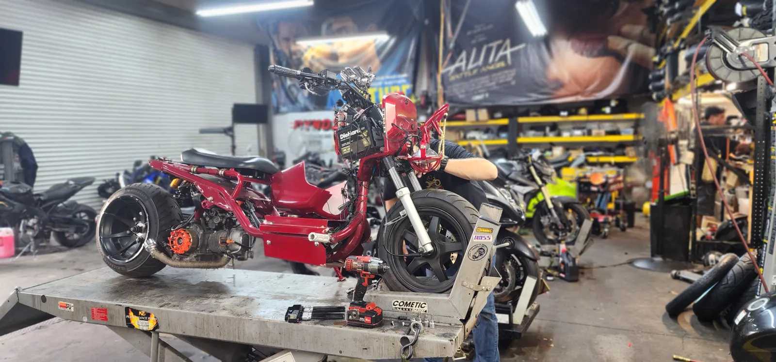 Motorcycle shop serving Mableton GA — a red custom Honda Ruckus strapped to a lift table with bodywork removed