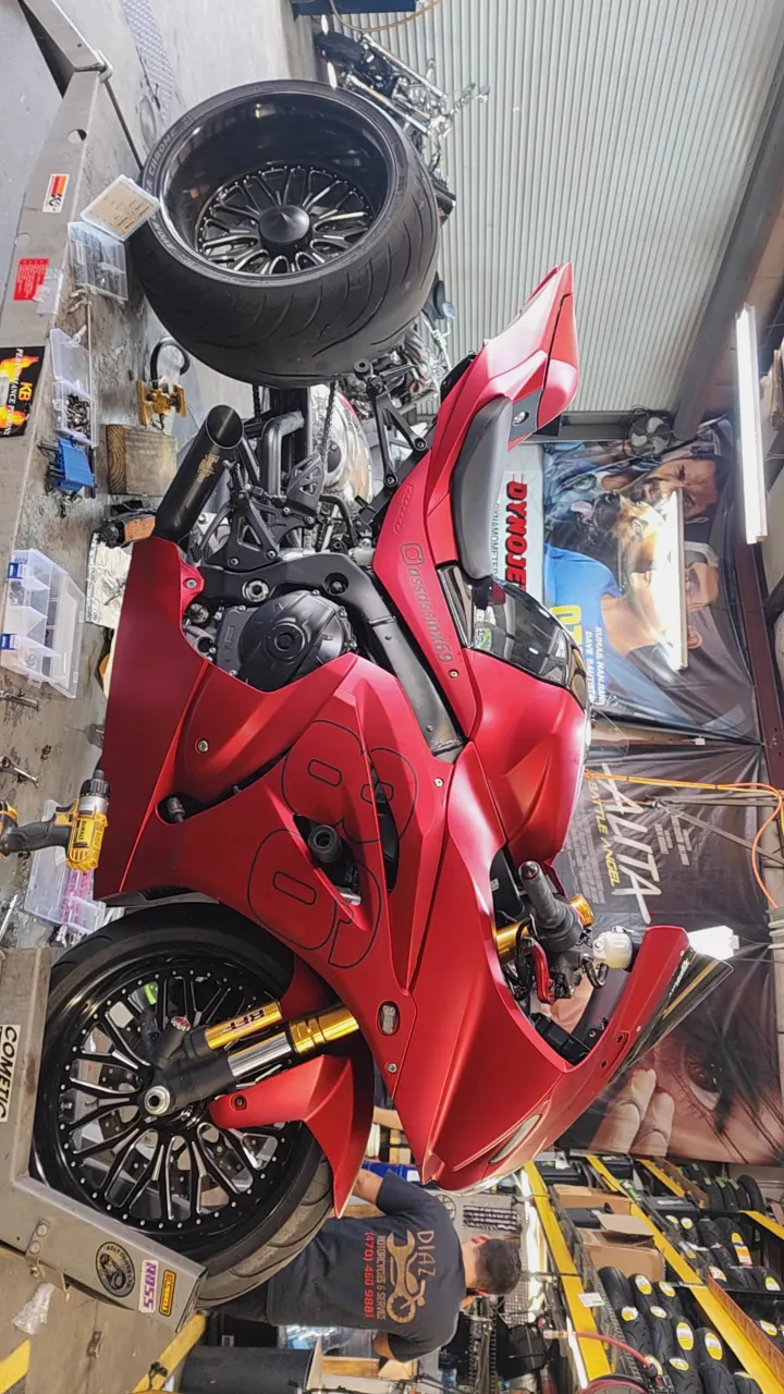 Motorcycle repair near Roswell — matte red fat-tire Suzuki GSX-R on the lift table, gold forks, tech at work