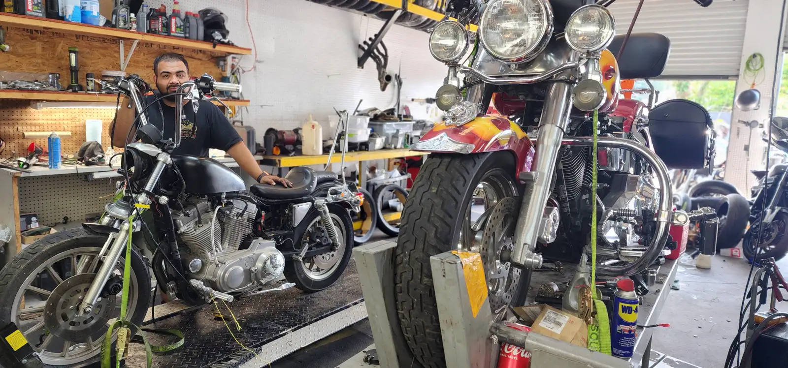 Motorcycle service Woodstock — technician standing between a bare Harley Sportster on a lift and a flame-painted cruiser