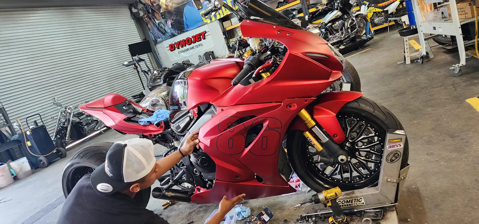 Motorcycle service cost Lawrenceville — tech crouched beside a matte-red Hayabusa on a lift with fairings partly removed.
