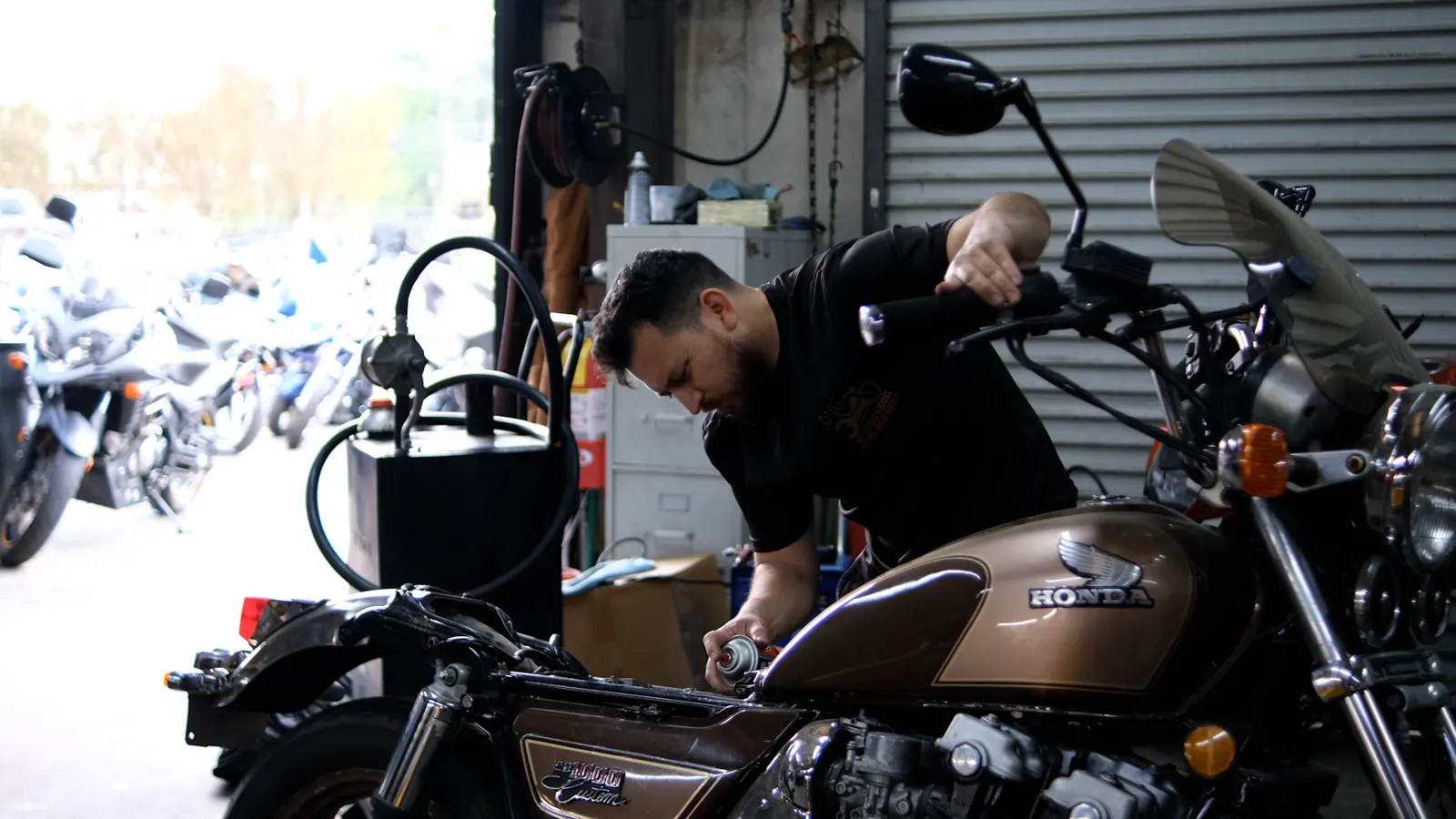 Motorcycle repair near Kennesaw — technician in a black Diaz shirt working on a brown Honda cruiser at the open bay door