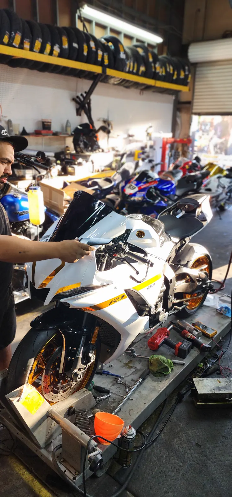 Motorcycle repair Kennesaw — tech in a cap works on a white Yamaha R1 with gold wheels up on the lift.