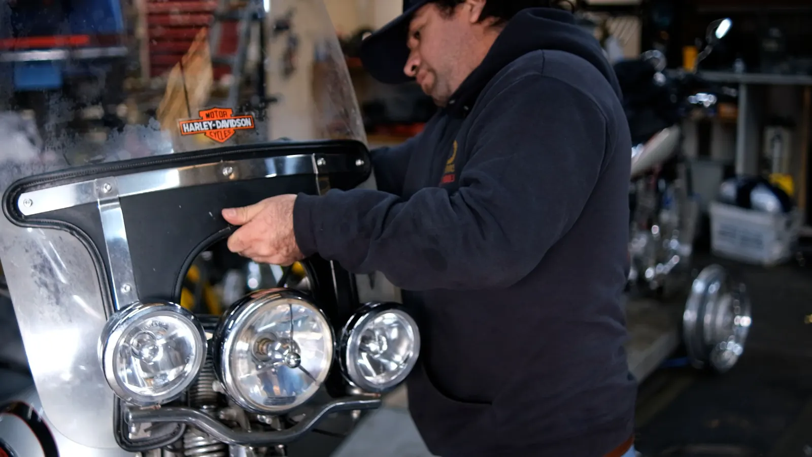 motorcycle service cost Kennesaw — technician in a Diaz hoodie fitting a bracket over a triple-headlight Harley front end