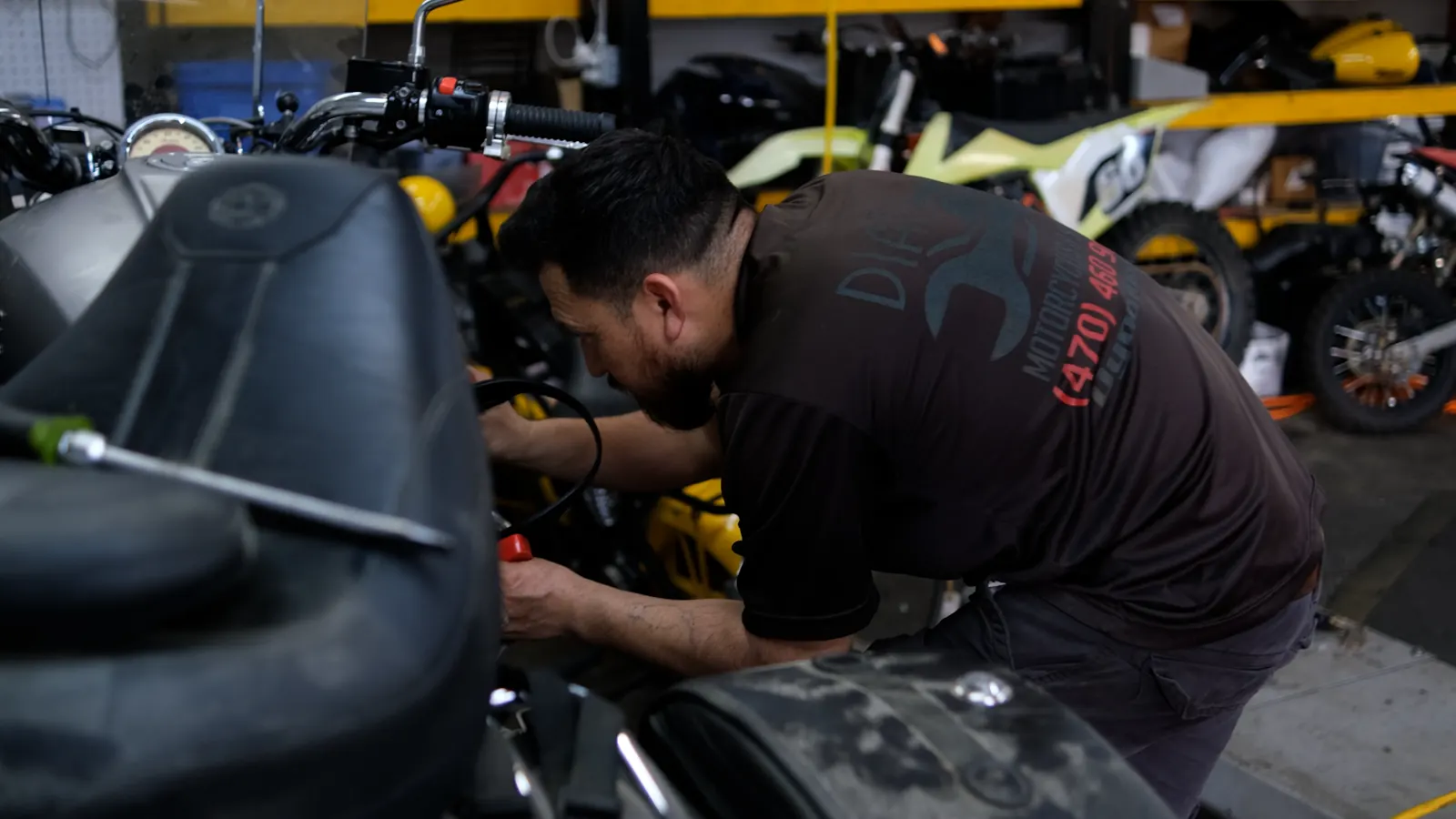 Dealer vs indie service Lawrenceville — technician in a Diaz shirt leaning over the bars working near the front controls