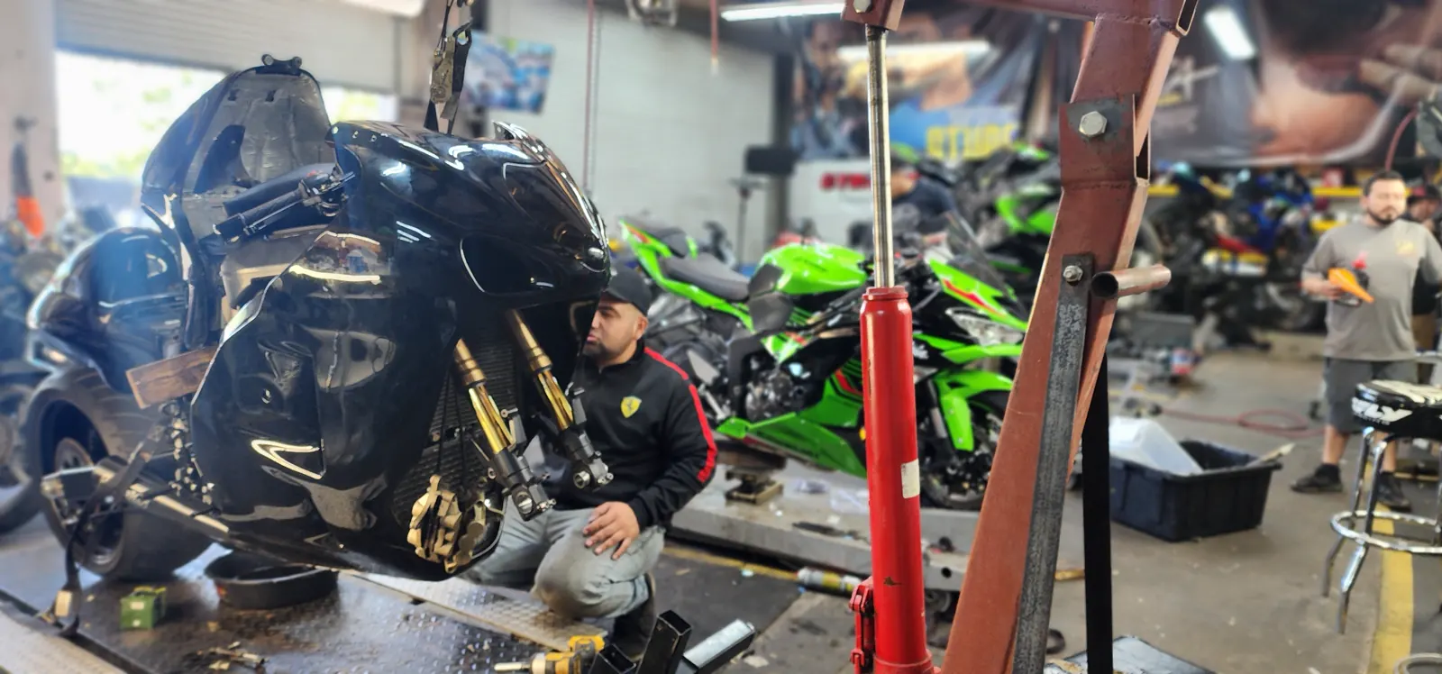 Motorcycle repair Smyrna — technician kneeling beside a black Suzuki Hayabusa on a hoist with front bodywork off
