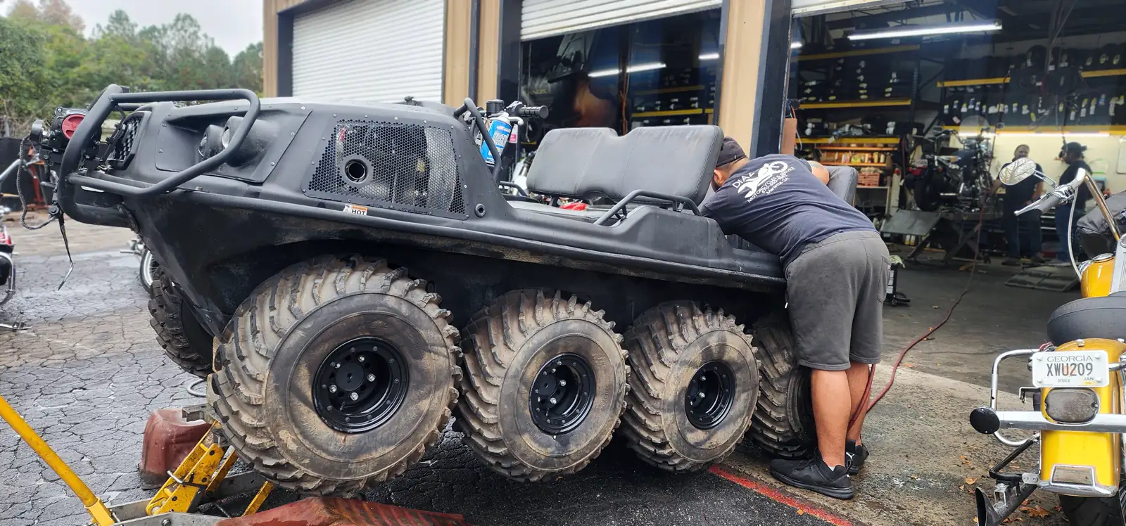 Newnan motorcycle service — a tech leaning into the cockpit of a black six-wheel Argo ATV outside the shop bays