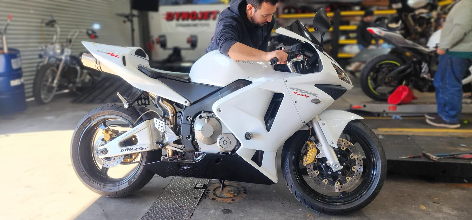 Motorcycle maintenance Newnan tuning — technician leaning over the handlebars of a white Honda CBR600RR near the dyno