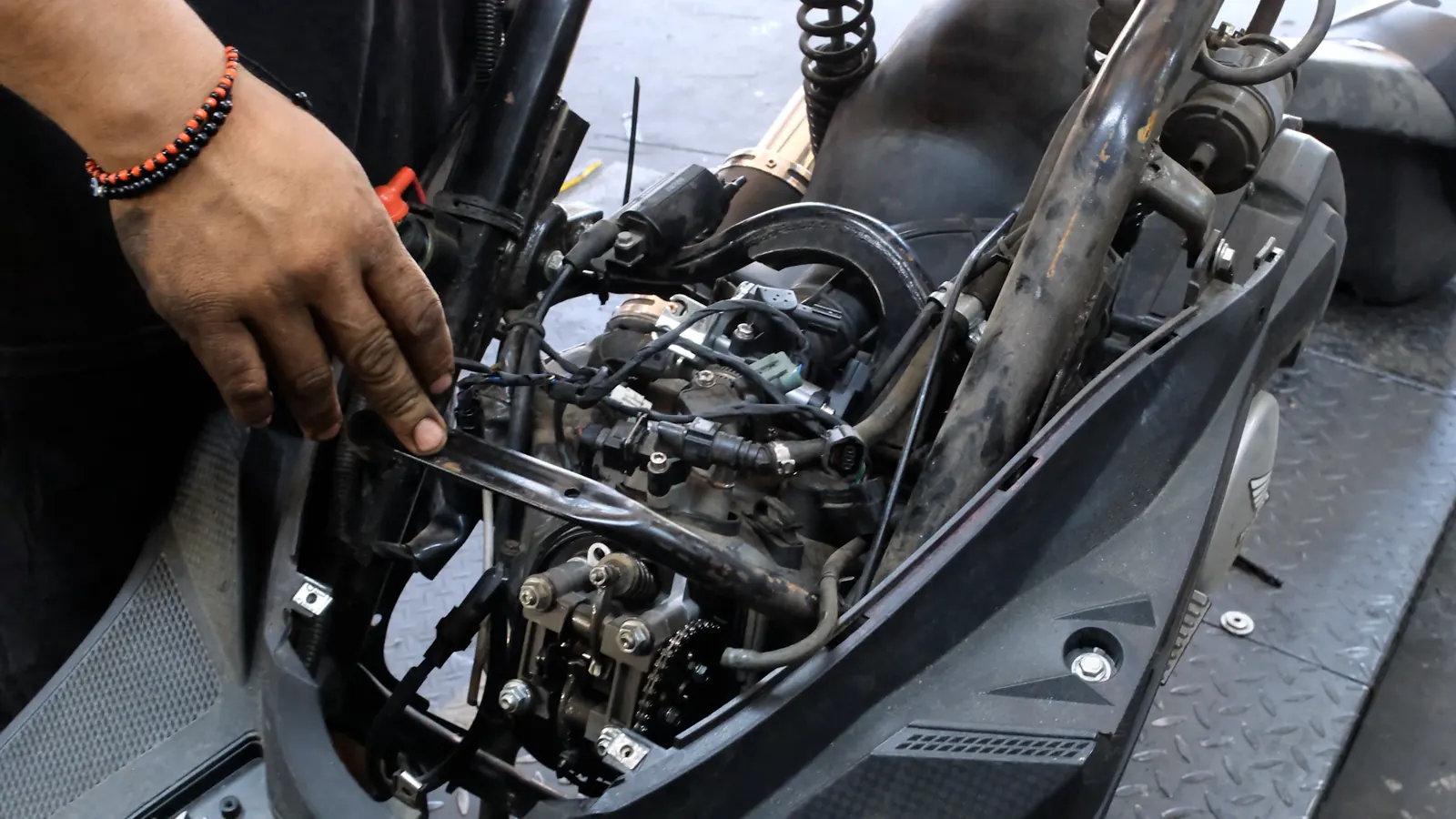 Motorcycle service Newnan — technician's hand at the exposed engine and throttle body of a scooter with panels off