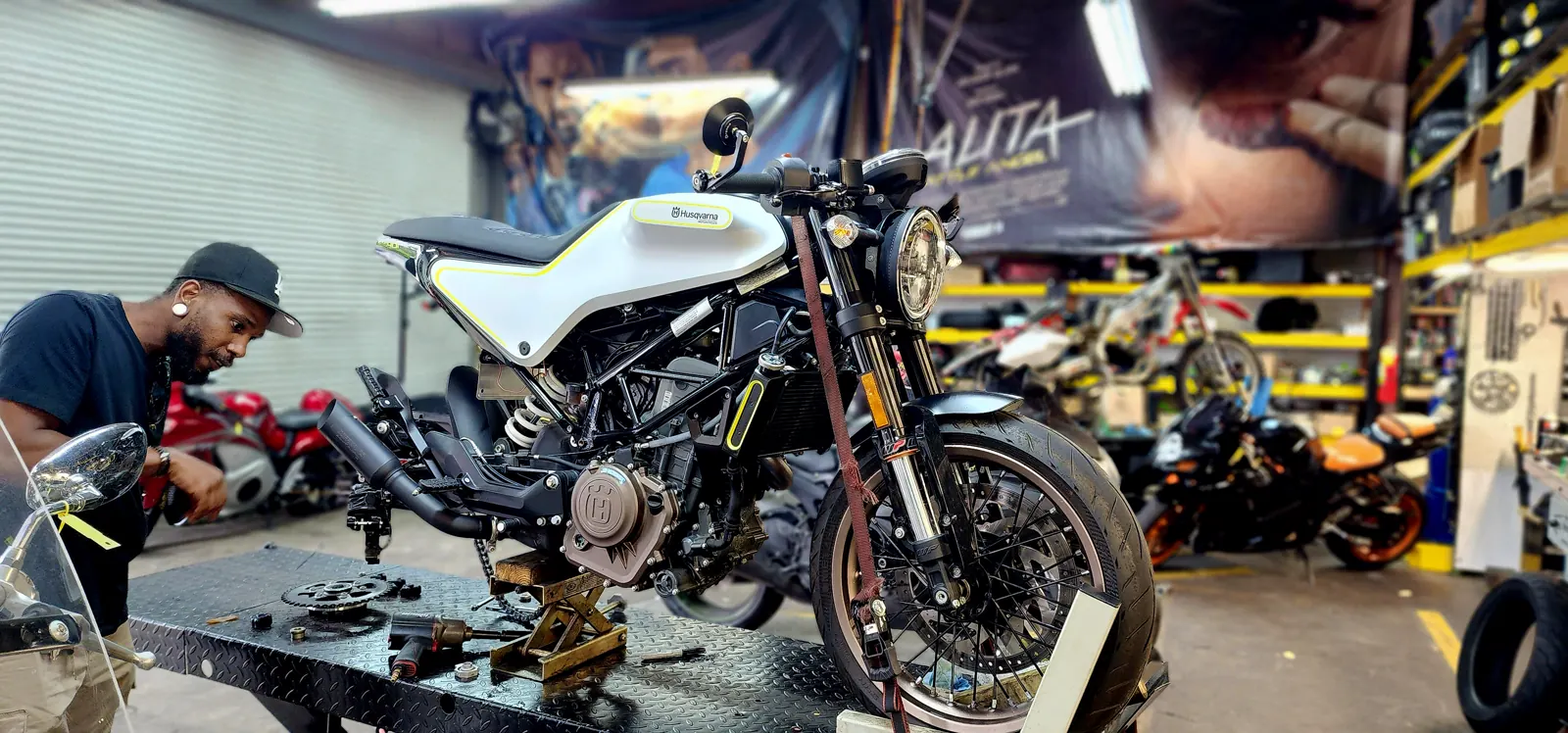 Motorcycle service in Dallas GA — tech beside a white Husqvarna Vitpilen with chain and gasket parts laid out