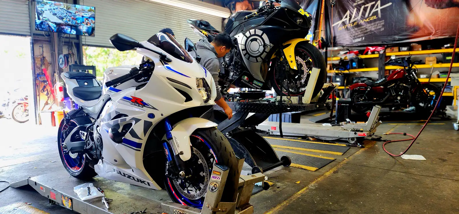 motorcycle maintenance Roswell — white and blue Suzuki GSX-R on a lift, a tech working a black and yellow R1 behind it