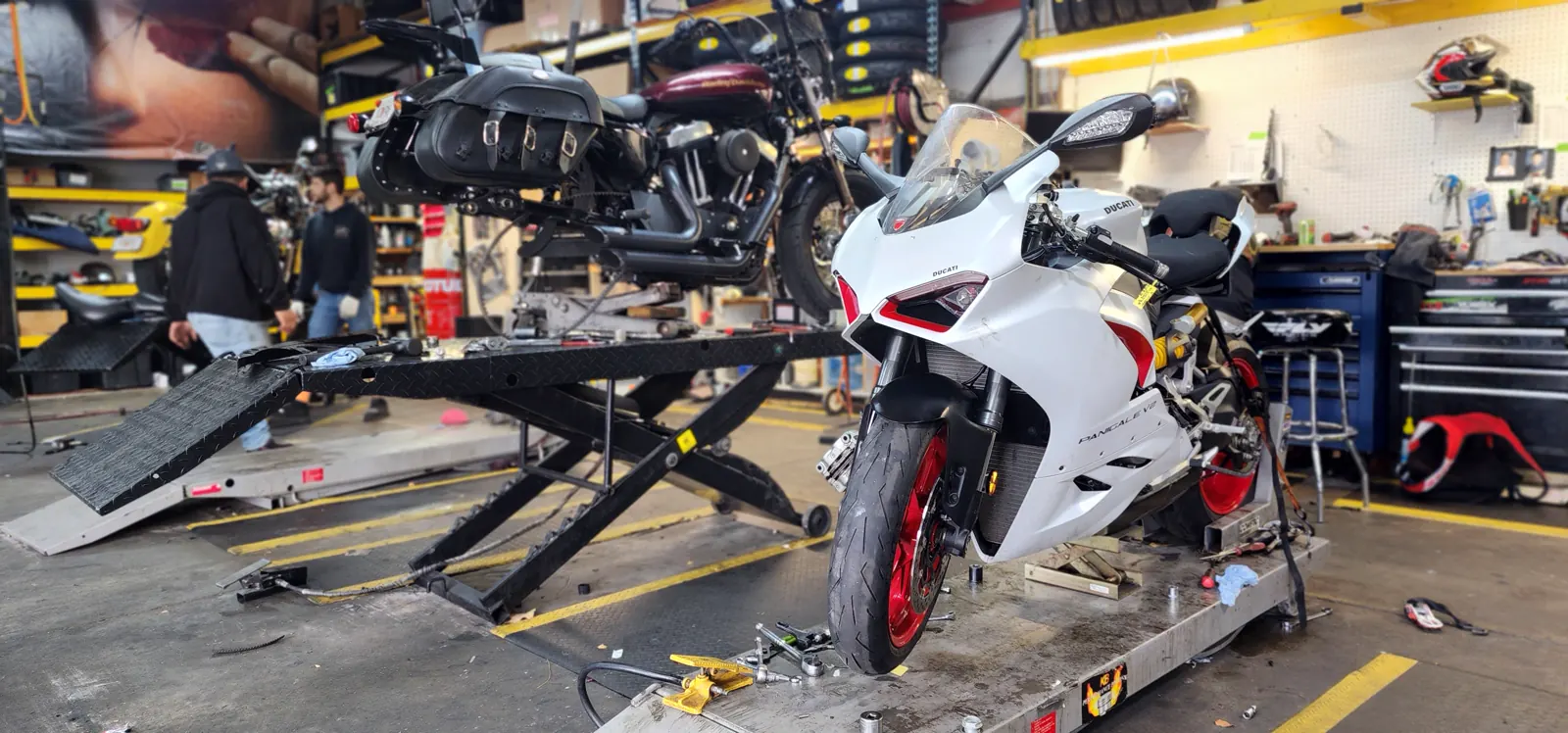 motorcycle service near Acworth GA — white Ducati Panigale with red wheels on a lift and a Harley Sportster raised behind