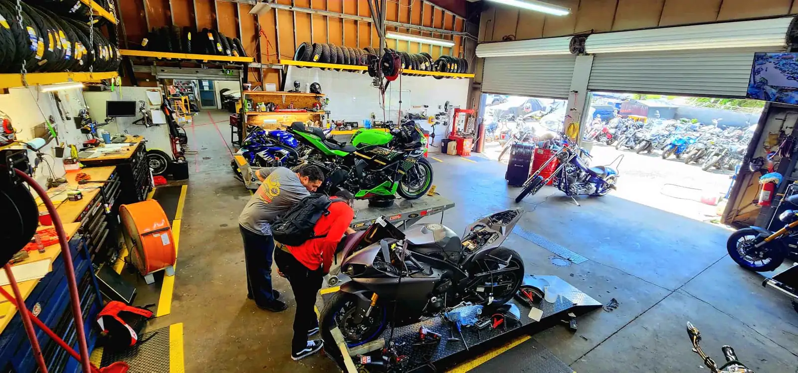 dealer vs indie service Douglasville — two techs working on a stripped black sportbike on a lift with tires racked overhead