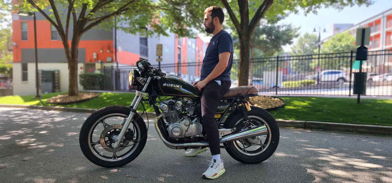 motorcycle restoration Smyrna — rider seated on a black and gold vintage Suzuki cafe racer in a mixed-use development