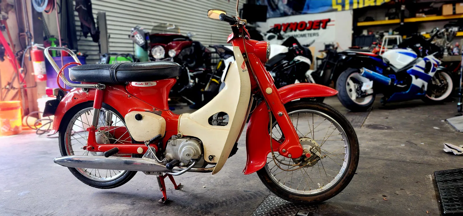 motorcycle sitting for years Smyrna — vintage red and cream Honda step-through revived and standing among modern sportbikes