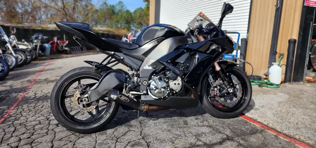 Black sport motorcycle parked on cracked asphalt near a building, with more bikes visible behind.