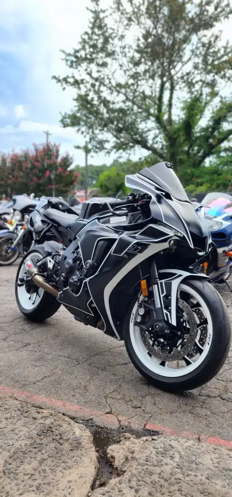 Black and white sport motorcycle parked outdoors, with other bikes and trees visible in the background.